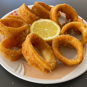 Calamares a la romana servidos en un plato con rebozado dorado y crujiente, acompañados de medio limón.