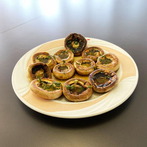 Champiñones enteros cocinados con salsa verde de ajo y perejil, servidos en un plato blanco sobre mesa oscura.