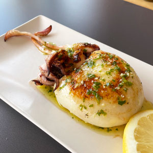 Sepia entera a la plancha con ajo y perejil, servida en plato rectangular con rodaja de limón.