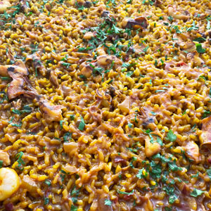 Arroz a banda con sepionet y gamba pelada, cocinado en fogón especial para paella, decorado con perejil fresco.