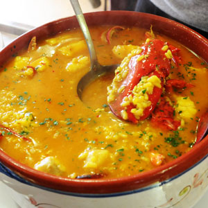 Arroz caldoso con bogavante servido en cazuela tradicional, con caldo dorado, arroz y trozos de marisco visibles, acompañado de cucharón.