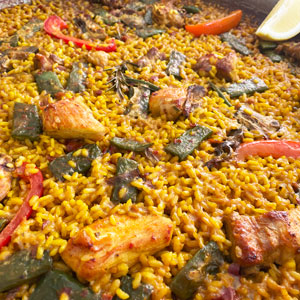 Arroz de montaña cocinado en fogones especiales para paella, con pollo, costilla y conejo, servido en paella tradicional y acompañado de alioli.