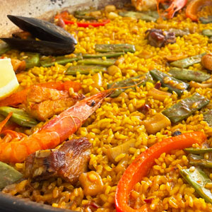Paella mixta con marisco, carne, judías verdes y pimiento rojo, cocinada en fogón especial para paellas y servida en recipiente tradicional.