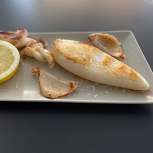 Calamar entero a la plancha servido en plato rectangular con sal en escamas y rodaja de limón.
