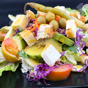 Ensalada de queso de cabra con lechugas variadas, tomate, pepino, col lombarda, zanahoria, aceitunas y guindilla, aliñada con salsa de níspero.
