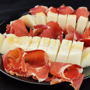 Plato con porciones de melón fresco y lonchas de jamón curado enrolladas, dispuestas de forma alterna sobre fondo negro.