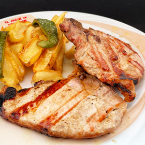 Chuletas de cerdo a la brasa servidas con patatas fritas y pimientos verdes como guarnición.