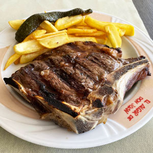 Chuletón de ternera gallega a la brasa con patatas fritas y pimiento verde.
