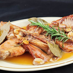 Plato de conejo espatarrat con ajos, laurel y romero sobre una salsa dorada.