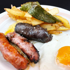 Plato de embutido de pueblo caliente con longaniza, morcilla, chorizo, patatas fritas y huevo frito.