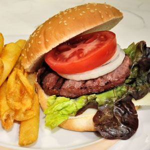 Hamburguesa clásica con carne a la brasa, lechuga, tomate, cebolla y pan de sésamo, acompañada de patatas fritas.