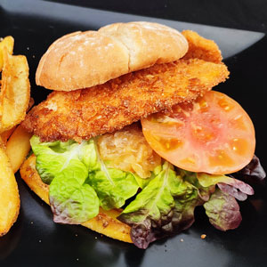 Hamburguesa de pollo empanado crujiente con lechuga, tomate, cebolla y pan rústico, servida con patatas fritas.