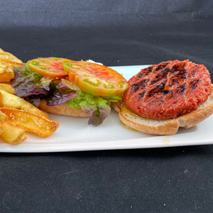 Hamburguesa vegana con pan rústico, lechuga, tomate, carne vegetal a la brasa y patatas fritas caseras.
