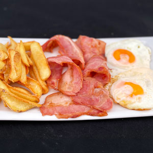 Plato con dos huevos fritos, tiras de bacon dorado y patatas fritas caseras.