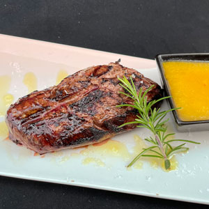 Magret de pato a la brasa acompañado de salsa de níspero servida aparte, decorado con romero fresco.