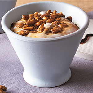 Postre helado de nata con nueces caramelizadas en vaso blanco