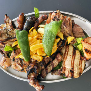 Parrillada de carne con piezas de pollo, cordero, ternera, cerdo y embutido, acompañada de guarnición de patatas fritas y pimientos verdes.