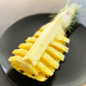 Rodajas de piña natural servidas en su cáscara sobre plato negro